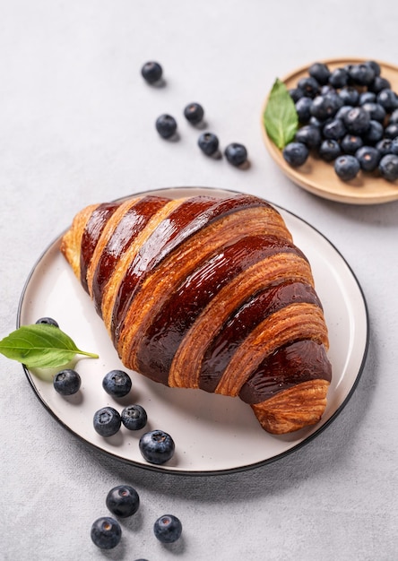 Freshly croissant with blueberries on a white plate on a light background Delicious homemade breakfast concept