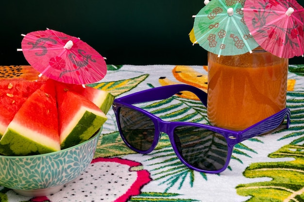 Freshly cut watermelon with a small umbrella, a glass of gazpacho and sunglasses, on top of a towel