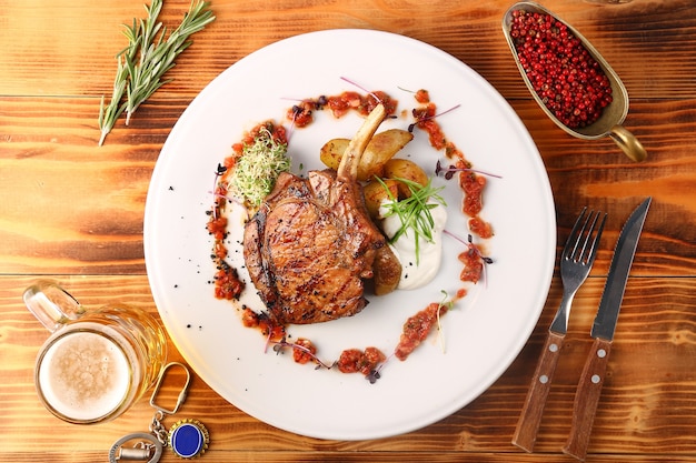 Photo freshly grilled hot steaks with potato on wooden table and beer in glass top view