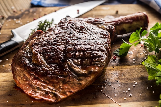 Freshly grilled tomahawk steak on slate plate with salt pepper rosemary and parsley herbs.