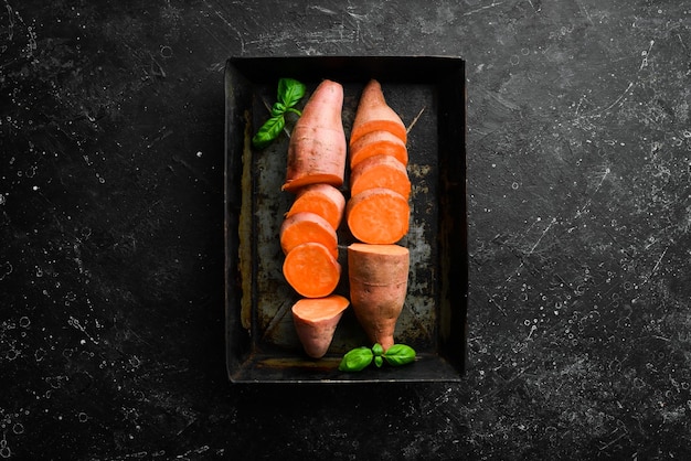 Freshly harvested organic sweet potatoes in a metal tray On a black background Top view Free space for your text