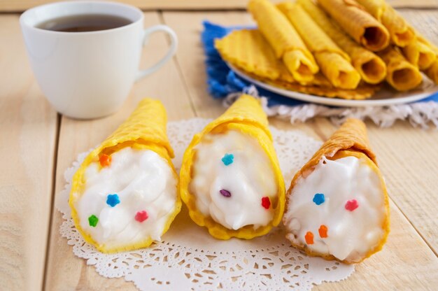 Cialde appena al miele intrecciate in un cono con una crema delicata su un tavolo di legno e una tazza di tè