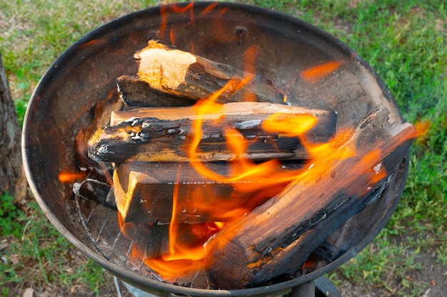 Freshly lit barbecue fire with logs of burning wood over small chips of kindling in a portable BBQ