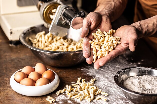 Freshly made gemelli pasta shapes with eggs and flour held in the hands of the chef.