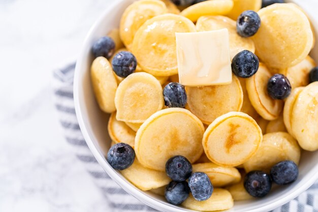 Freshly made mini pancake cereal with fresh blueberries in a white bowl.