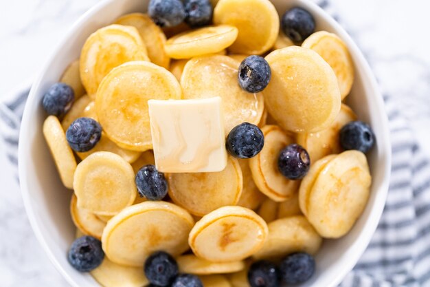 Freshly made mini pancake cereal with fresh blueberries in a white bowl.