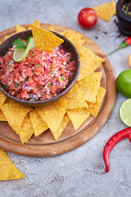 Freshly made salsa dip sauce with nacho chips on wooden board