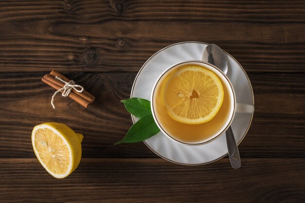 Tè appena fatto, bastoncini di cannella e limone su un tavolo di legno. la vista dall'alto. una bevanda tonificante utile per la salute.