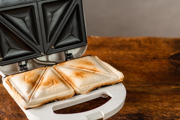 Freshly made toasted sandwiches in a sandwich maker on a wooden background Morning breakfast concept