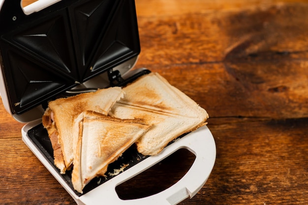 Freshly made toasted sandwiches in a sandwich maker on a wooden background Toasted triangular sandwiches with cheese