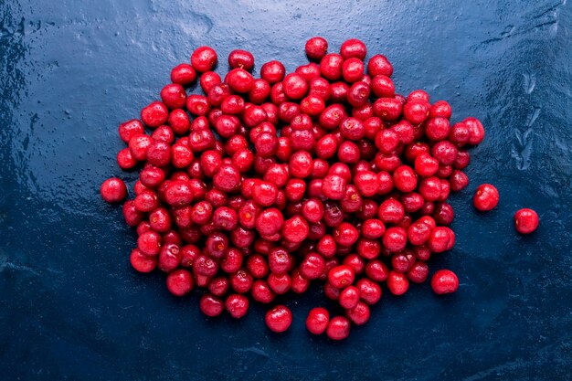 Freshly picked cherries with droplets of dew and water on a wet dark blue background.