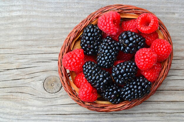 Freshly picked organic blackberries and raspberries in a basket on old wooden table.Healthy eating,vegan food or diet concept.Selective focus.