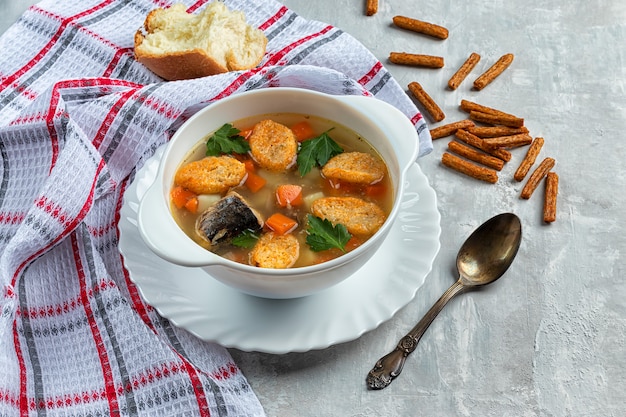 Freshly prepared canned tuna soup with crackers on a concrete background with herbs