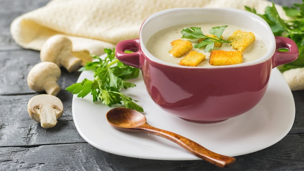 Freshly prepared cream soup of mushrooms with croutons on a white plate with a wooden spoon