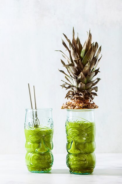 Свежеприготовленный зеленый ананасовый смузи в очках с лицами. Концепция здорового утреннего завтрака.