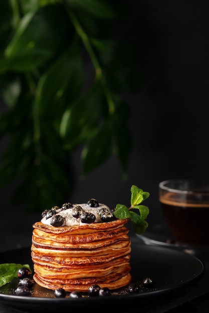 Freshly prepared homemade pancakes with sour cream and fresh\
berries, decorated with food gold with a cup of fragrant\
coffee