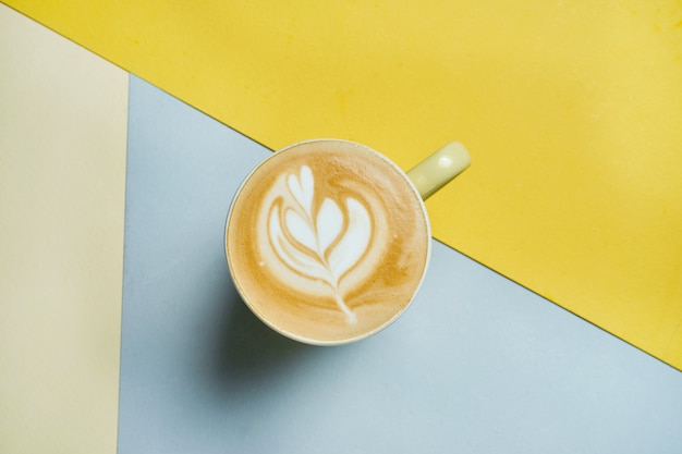 Freshly prepared latte with layers of milk, coffee and foam in a yellow glass on a colored surface Coffee picture for menu