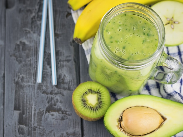 A freshly prepared smoothie of avocado, banana and lemon with blue cocktail straws on a rustic table