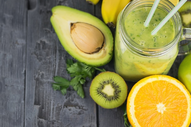 A freshly prepared smoothie of avocado, banana, orange, lemon and kiwi on a dark wooden table. Diet vegetarian food.