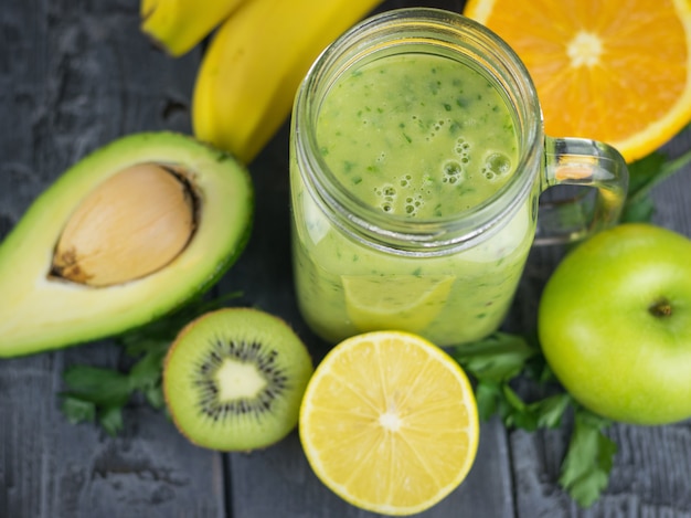 Un frullato appena preparato di avocado, banana, arancia, limone e kiwi su un tavolo di legno. dieta cibo vegetariano.