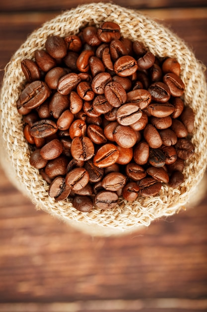 Freshly roasted aromatic coffee in a burlap bag on a wooden surface