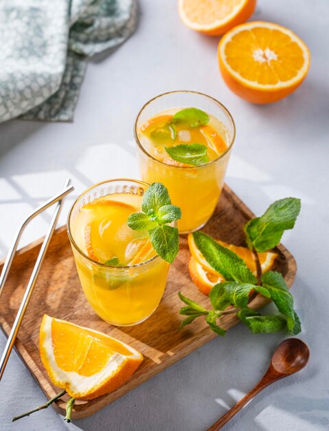 Freshly squeezed juice in a glass with fresh oranges mint and ice on a light background with metallic tube and shadow healthy citrus detox drink for breakfast