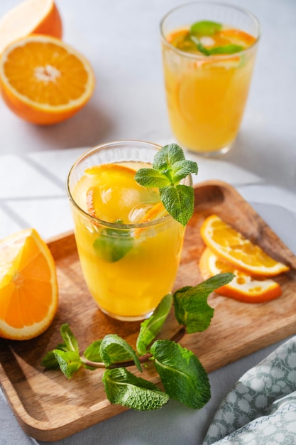 Freshly squeezed juice in a glass with fresh oranges mint and ice on a light background with metallic tube and shadow