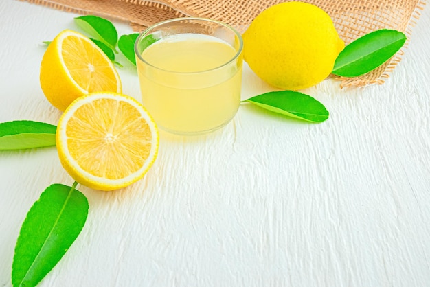 Свежевыжатый лимонный сок в маленькой мискеКуча лимонов на деревянном столе