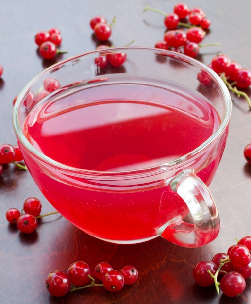 Freshly squeezed red juice, and bunches of red currants on a wooden table closeup