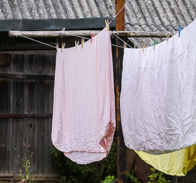 屋外のロープにぶら下がっている洗いたてのベッドリネン。田舎の庭で衣類を乾燥させます。