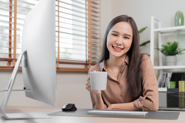 신선하고 아름다운 아시아 젊은 비즈니스 여성이 컵 커피를 들고 있거나 집에 앉아 PC 컴퓨팅 작업을 하는 프리랜서를 마시는 covid19의 집에서 일하는 사회적 거리