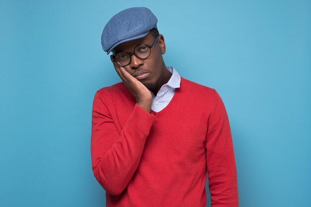 Фрикано-американский студент колледжа в красном свитере и синей шляпе устал и скучает