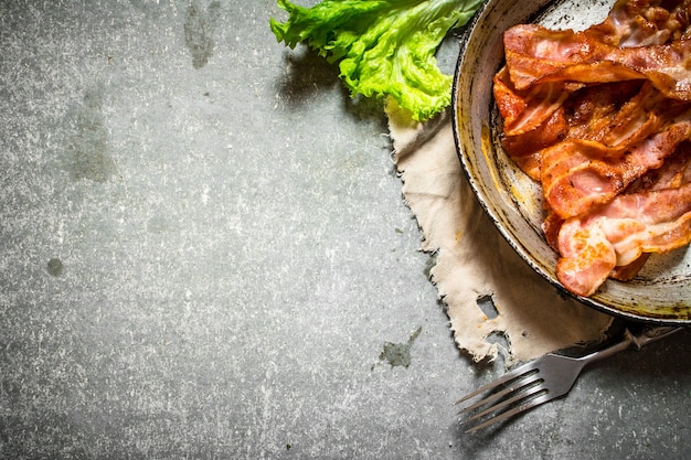 Fried bacon and greens. On a stone table.