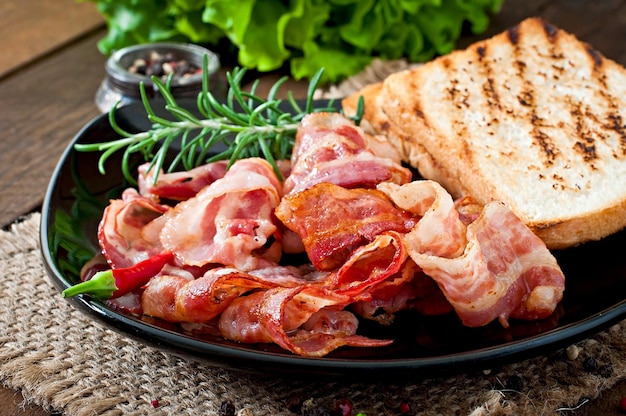 Fried bacon and toast on a black plate on a wooden background