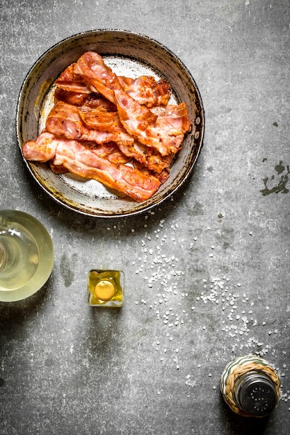 Fried bacon with oil and salt. On a stone background.