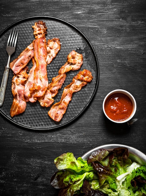 Fried bacon with sauce and greens. On a black wooden background.