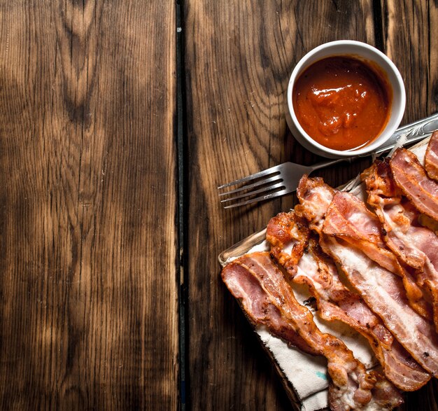 Fried bacon with tomato sauce. On a wooden background.