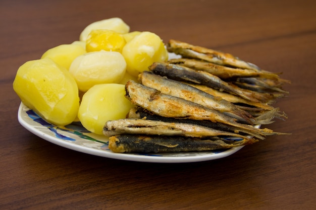 Fried baltic herring with boiled potatoes on a plate on wooden background