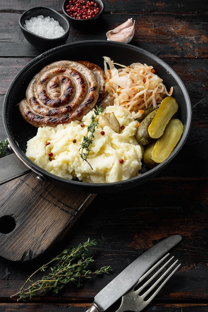 Fried Bavarian German NÃ¼rnberger sausages with sauerkraut, mashed potatoes in cast iron frying pan, on old dark  wooden table background