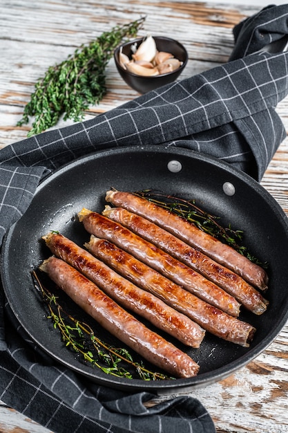 イタリアのハーブとチーズを入れたフライパンで揚げた牛肉と豚肉のソーセージ。白い木の背景。上面図。