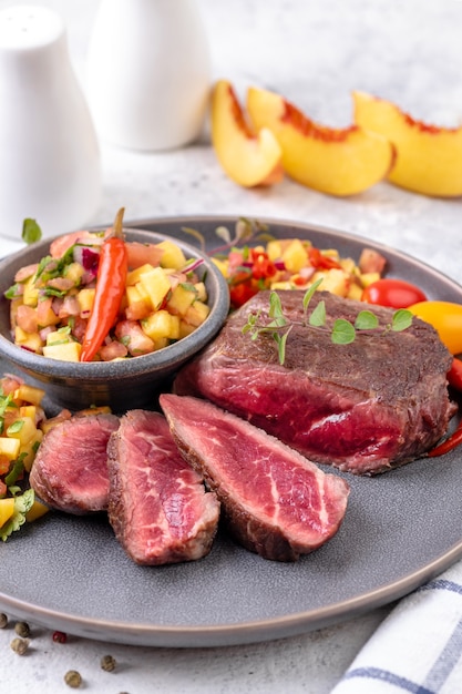 Fried beef steak with peach fruit salsa, tomato and chili. Medium or Rare fried steak cut into pieces. Ready to eat. Close-up.