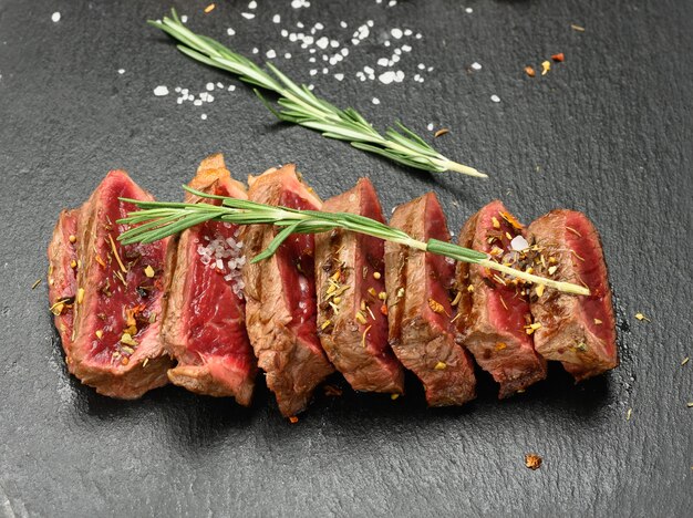 Fried beef steaks cut into pieces on a black board, the degree of doneness rare with blood, close up