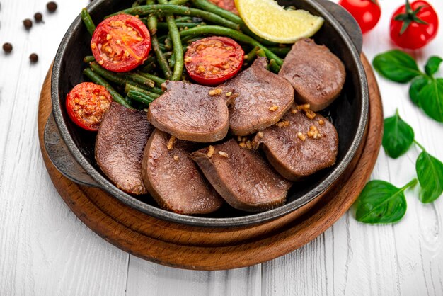 Fried beef tongue with green beans and tomatoes in a pan