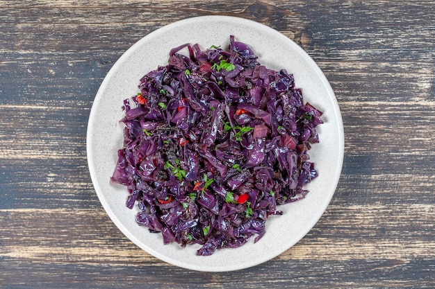 Fried blue cabbage with onion apple and garlic in plate on wooden table Top view closeup