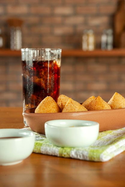 Fried brazilian croquettes coxinha de frango with iced soda in a kitchen with bricks wall
