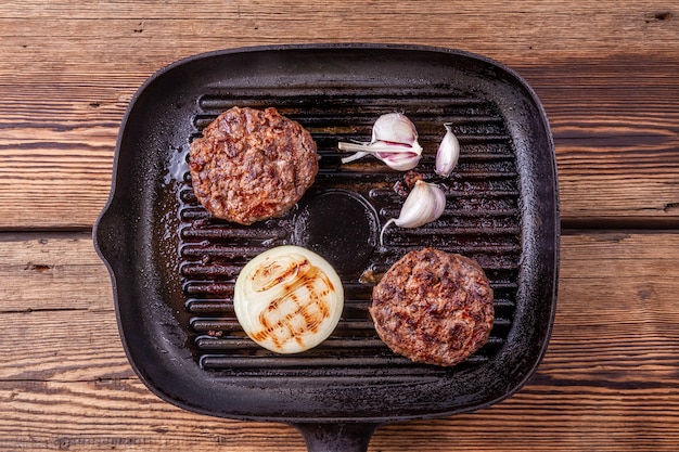 Fried burger beef cutlets with onion and garlic on grill pan on wooden background