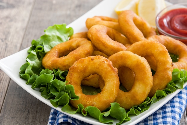 Fried calamari rings with lettuce and ketchup on wooden surface