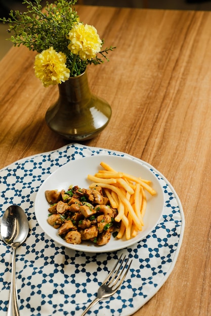 Жареные кальмары с ложкой и вилкой для картофеля фри подаются в блюде, изолированном на столе, вид на закуску фастфуда