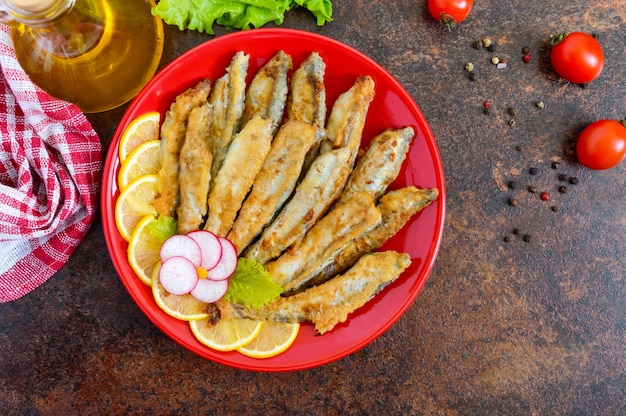 Fried capelin with lemon on a red plate. A dish of small sea fish. Top view. Flat lay