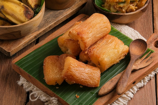 Fried cassava is served on a cutting board with a banana leaf base. Arranged in such a way with a classic kitchen table theme